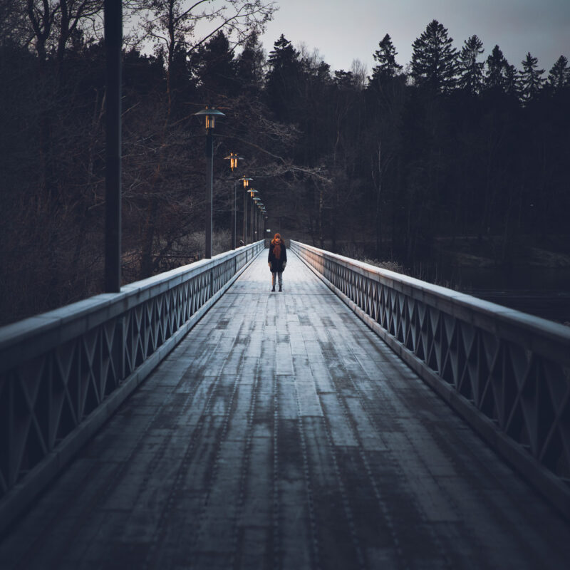 En kvinna står på mitten av en lång bro precis innan solen har gått upp.